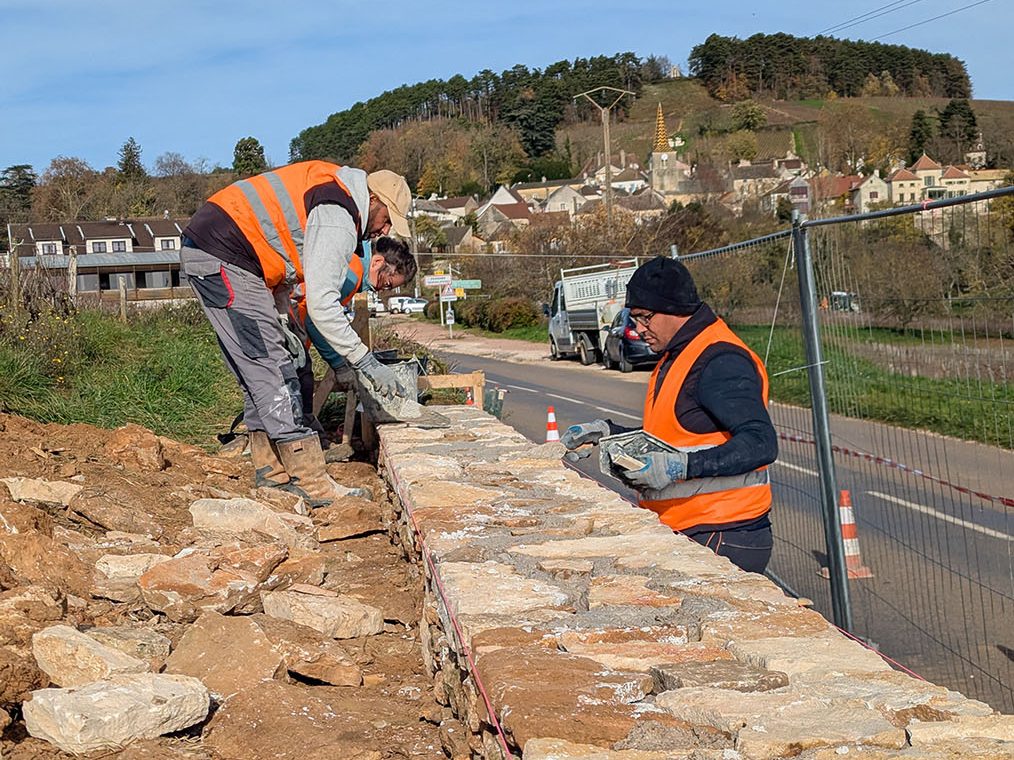 muraillers travaillant sur un mur en pierre maçonné le long d'une route passante, Pernand Vergelesses, France